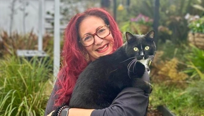 Smiling woman holding a black and white cat outdoors, representing compassion for animals at Beyond Animal Research.