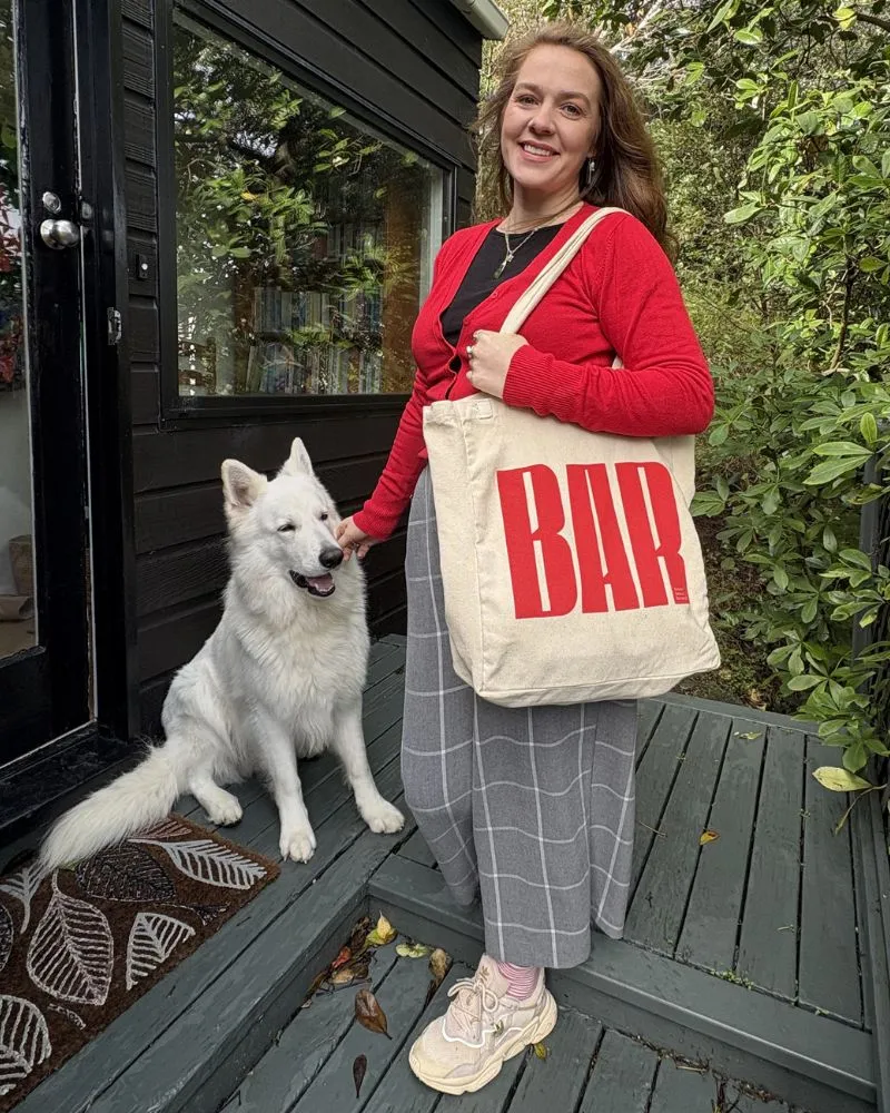 Person outdoors smiling while holding a Beyond Animal Research tote bag with the red BAR logo, symbolising advocacy for animals in science.