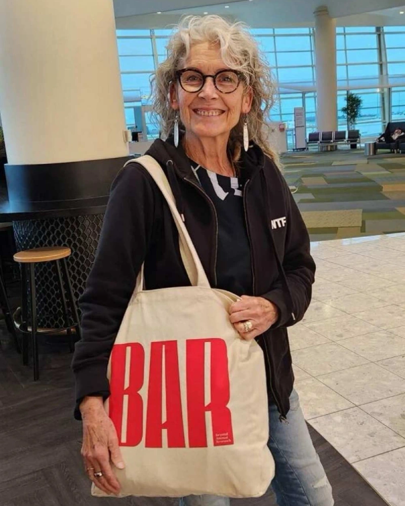 Person smiling and holding a Beyond Animal Research tote bag with bold red BAR logo at an airport, representing support for ethical science.